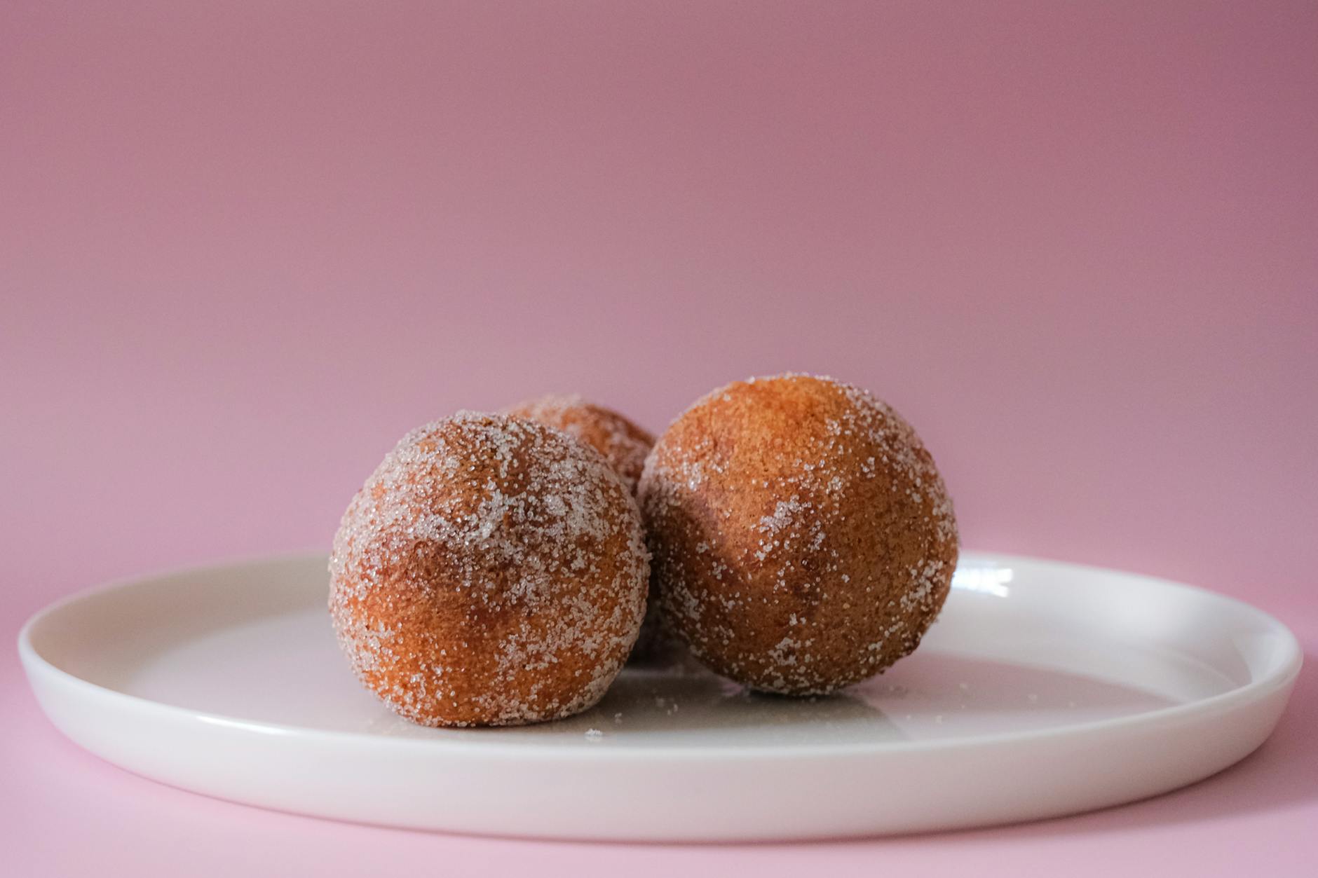 Kulki ciasta w cukrze na białym talerzu na różowym tle